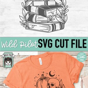 May include: Orange t-shirt featuring a black and white graphic design. The design includes a pumpkin, skull, books, stars, and a crescent moon. The text "Wild Pilot SVG CUT FILE" is also visible.
