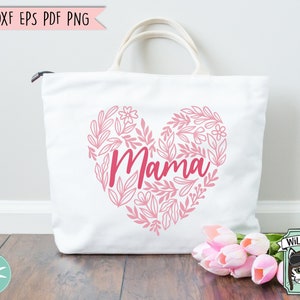 Pu&ograve; includere: Borsa tote bianca con un design a cuore floreale rosa e la parola "Mama" in lettere rosa.