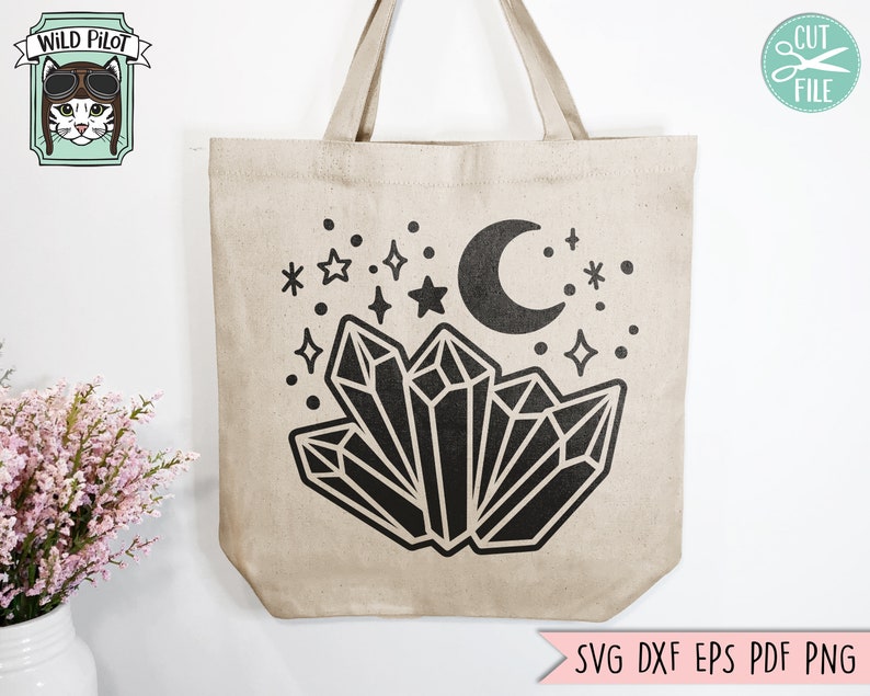 May include: A beige tote bag with a black design of crystals, a crescent moon, and stars. The design is centered on the bag.