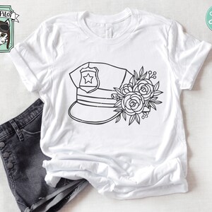 Puede incluir: Un dise&ntilde;o en blanco y negro de l&iacute;nea de arte de un sombrero de polic&iacute;a con una estrella en la parte delantera y un arreglo floral en el lateral. El dise&ntilde;o est&aacute; en una camiseta blanca.