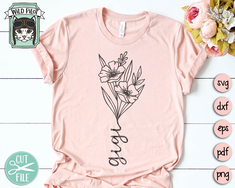 May include: A pink t-shirt with a black line drawing of a bouquet of flowers and the word "grow" written vertically. The shirt is on a white wooden surface.