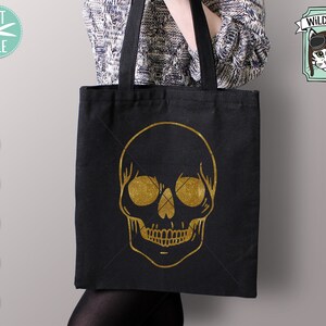 May include: A black tote bag with a gold glitter skull design. The bag has a long handle and is made of canvas.