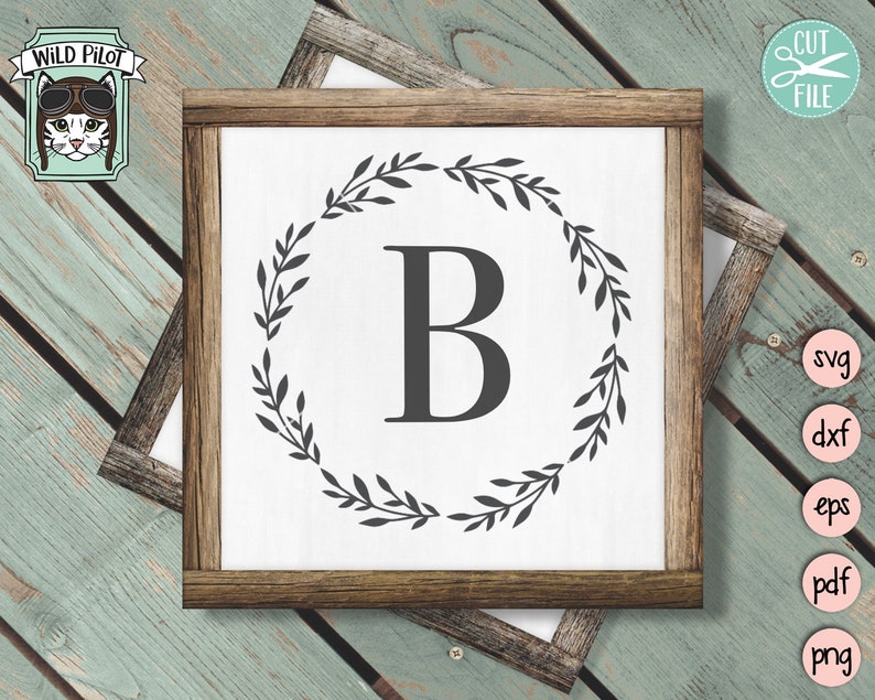 May include: A white sign with a brown wooden frame, featuring a black wreath with leaves and the letter "B" in the center.