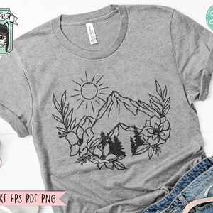 May include: A gray t-shirt with a black line drawing of a mountain range, sun, and flowers. The text "Wild Pilot" is in a box in the top left corner of the image.