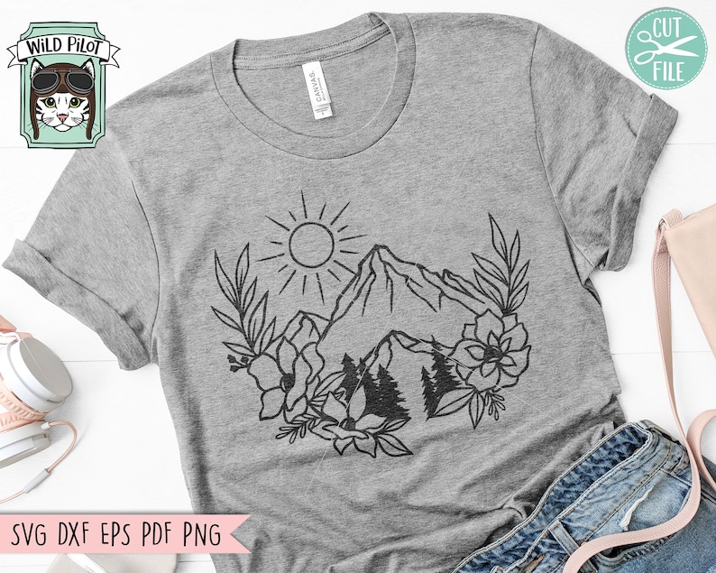 May include: A gray t-shirt with a black line drawing of a mountain range, sun, and flowers. The text "Wild Pilot" is in a box in the top left corner of the image.