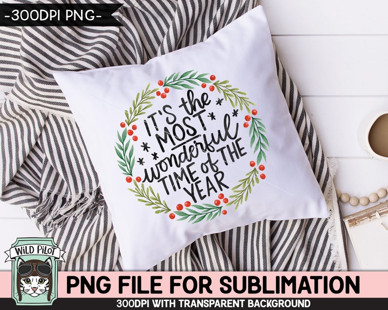 May include: White square pillow with the text "It's the MOST wonderful TIME OF THE YEAR" in black script, surrounded by a green wreath with red berries. The pillow is on a striped blanket.