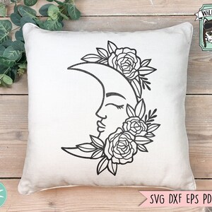 May include: A white pillow with a black line drawing of a crescent moon with a face and floral details. The moon is surrounded by flowers and leaves.