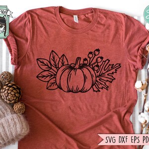 May include: A black and white line drawing of a pumpkin with leaves and berries. The image is on a red t-shirt.