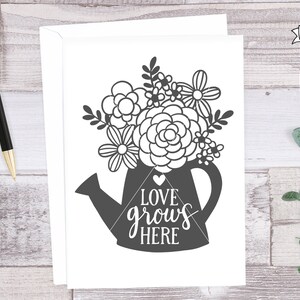 May include: A black and white printable design of a watering can with flowers and the text "Love grows here".