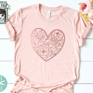 May include: A pink t-shirt with a rose gold floral heart design. The design is a heart shape with flowers and leaves inside. The shirt is laying flat on a white surface.
