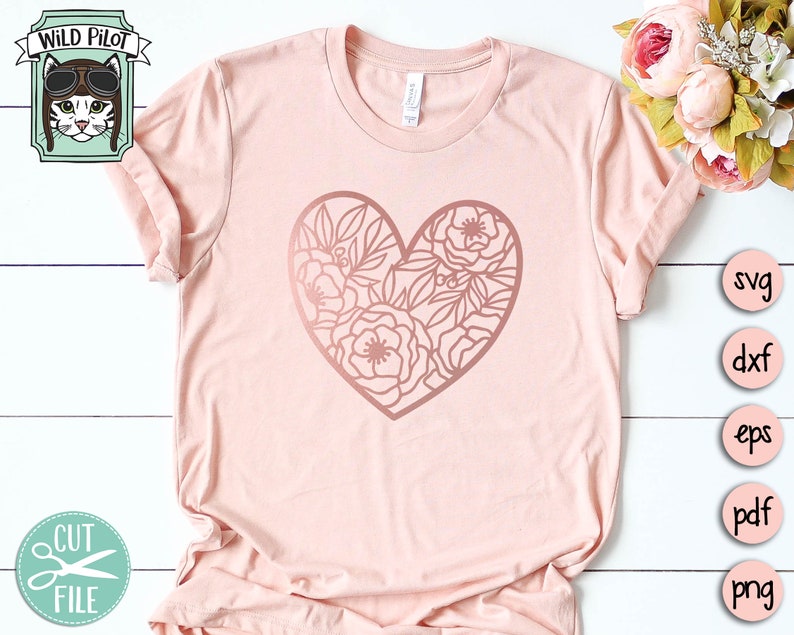 May include: A pink t-shirt with a rose gold floral heart design. The design is a heart shape with flowers and leaves inside. The shirt is laying flat on a white surface.