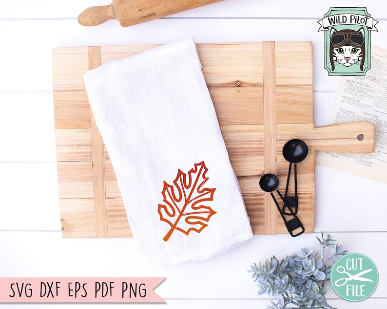 May include: A white kitchen towel with a red-orange maple leaf design. The towel is on a wooden cutting board with two black measuring spoons. The text "SVG DXF EPS PDF PNG" is at the bottom of the image.