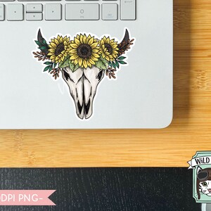 May include: A sticker featuring a white bull skull with a floral crown of yellow sunflowers and green leaves. The sticker is on a laptop.