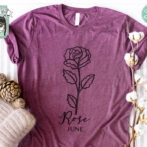 May include: A purple t-shirt with a black outline of a rose and the text "Rose June".