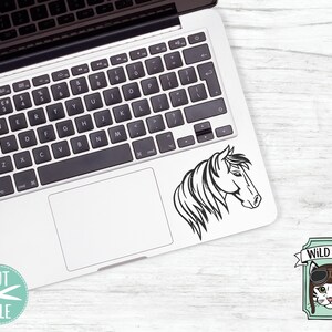 May include: A black and white line art illustration of a horse's head. The image is on a laptop screen. The laptop is on a white wooden surface. There are five circles with text in them: svg, dxf, eps, pdf, and png. Below the circles is a cartoon image of a cat wearing aviator goggles with the text "WILD PILOT" above the cat.