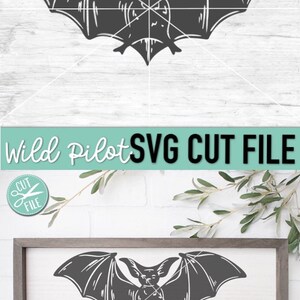 May include: A black and white silhouette of a bat with its wings spread wide. The bat is in a flying position. The image is on a white background with a wooden frame.