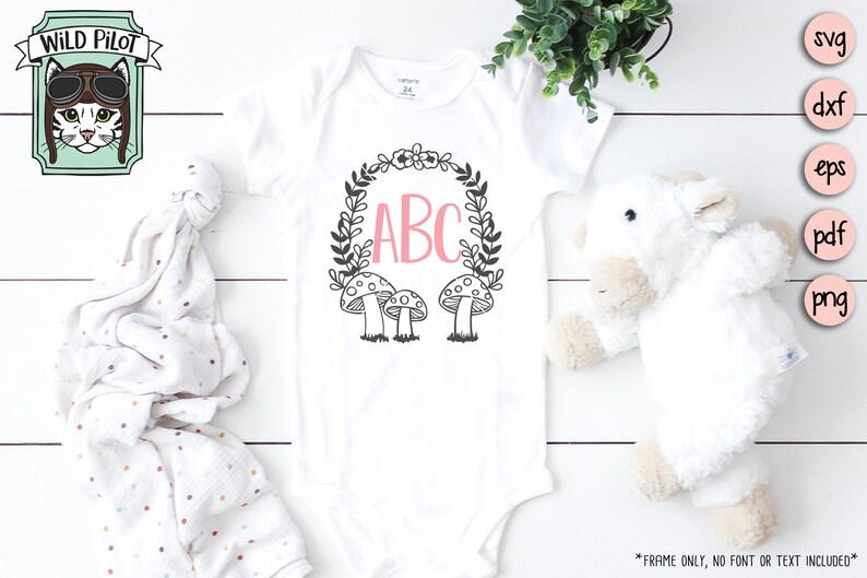 Op de afbeelding: Een witte romper met een zwart-witte kransontwerp met paddenstoelen en de letters ABC in roze. De romper ligt op een witte houten achtergrond.