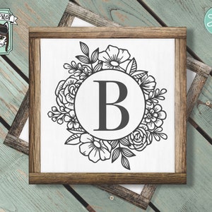 May include: A black and white floral wreath with a circle in the center containing the letter "B".