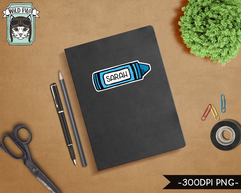 Peut inclure: Un carnet noir avec un autocollant de crayon bleu qui dit "SARAH" dessus. Le carnet est sur une surface brune avec une paire de ciseaux, deux stylos et quelques trombones.