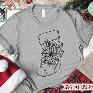 May include: A black and white line drawing of a Christmas stocking with a poinsettia flower on a grey t-shirt. The text "SVG DXF EPS PDF PNG" is at the bottom of the image.
