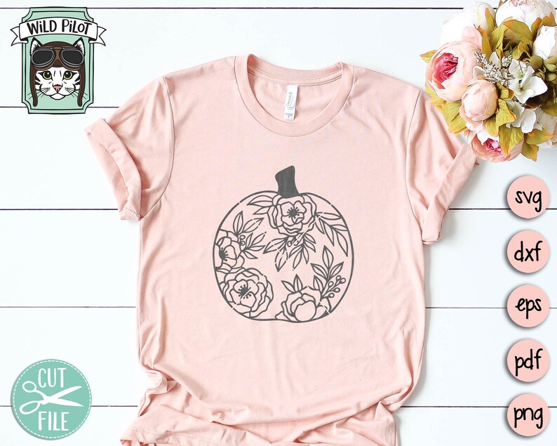 Op de afbeelding: Een roze T-shirt met een zwart bloemig pompoenontwerp. Het ontwerp is zwart omlijnd en bevat een steel en bladeren. Het shirt is een populaire keuze voor herfstmode.