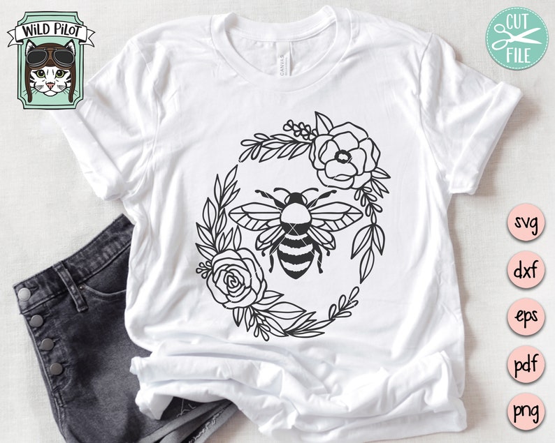Puede incluir: Una camiseta blanca con un dise&ntilde;o en blanco y negro de una abeja rodeada de flores. El dise&ntilde;o tiene forma circular.
