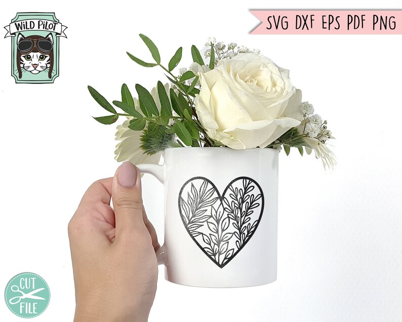 May include: A white ceramic mug with a black outline of a heart filled with leafy branches. The mug is holding a bouquet of white roses and greenery.