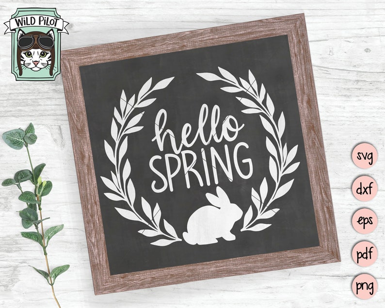 Op de afbeelding: Een zwart schoolbord met een witte krans, de tekst "hello spring" en een wit silhouet van een konijn. Het schoolbord is omlijst met hout.