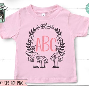 Op de afbeelding: Een roze baby-onesie met een zwart-witte krans met de letters ABC in roze erin. Er zijn drie zwart-witte paddenstoelen onderaan de krans.