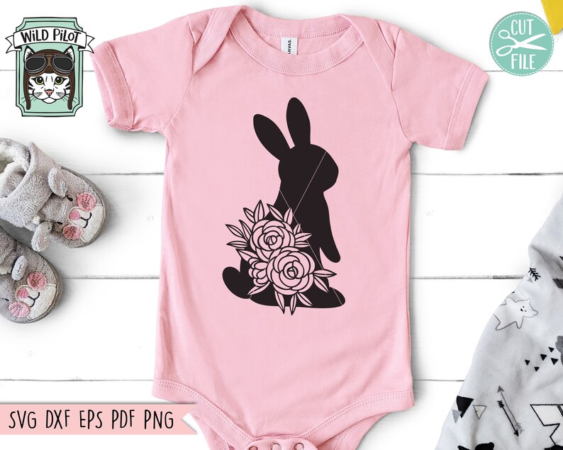 Op de afbeelding: Een lichtroze babyromper met een zwart silhouet van een konijn met bloemen. De romper heeft korte mouwen en een ronde hals. De tekst "SVG DXF EPS PDF PNG" staat onderaan. Een "Wild Pilot"-logo staat linksboven.