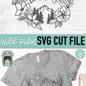 May include: A black and white line art design of a mountain range with a sun and flowers. The design is on a gray t-shirt. The text "Wild Pilot SVG CUT FILE" is at the top of the image.