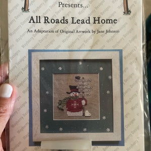 May include: A cross-stitch pattern featuring a snowman with a red sweater and a sign that reads "All Roads Lead Home". The pattern is titled "Mayberry Designs Presents... All Roads Lead Home" and includes a small bag of beads.