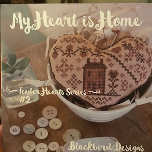 May include: A cross-stitch pattern for a heart-shaped design with a house inside. The pattern is titled "My Heart is Home" and is part of the "Tender Hearts Series #2". The pattern is by Blackbird Designs.
