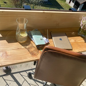 May include: A wooden desk with a brown leather chair, a glass pitcher of water, a tablet, and two notebooks. The desk is attached to a balcony railing.