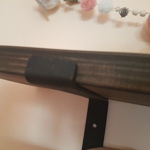 Puede incluir: Una estanter&iacute;a de madera te&ntilde;ida oscura con un soporte de metal negro fijado a una pared blanca. Una guirnalda decorativa con pompones rosas, grises y blancos y p&aacute;jaros de fieltro cuelga sobre la estanter&iacute;a. La estanter&iacute;a est&aacute; soportada por un soporte de metal negro.