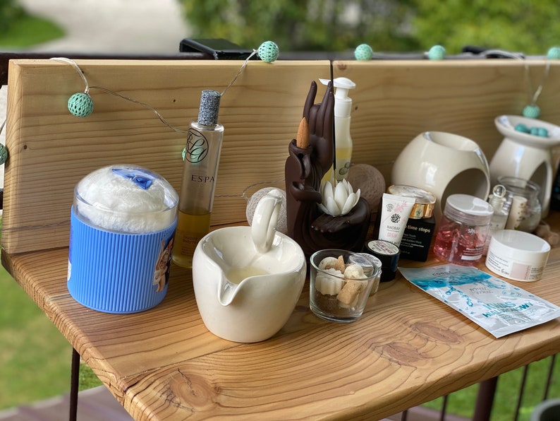 May include: A wooden shelf with a variety of spa and beauty products, including a bottle of ESPA body oil, a white ceramic bowl, a blue and white striped container, and a small glass jar filled with white beads. There are also several small bottles of essential oils and a white jar of cream.