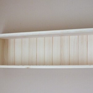 Peut inclure: Une étagère en bois blanc au design simple. L'étagère est rectangulaire et en bois brut.