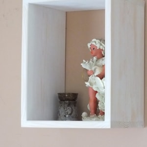 May include: A white wooden shadow box with a small porcelain figurine of an angel holding a flower and a small decorative bowl inside.