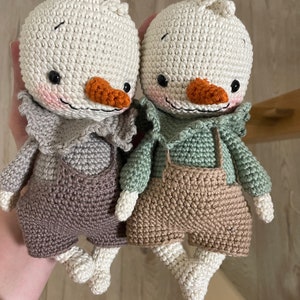 May include: Two crocheted stuffed toys shaped like birds with brown and beige overalls. One bird has a green shirt and the other has a brown shirt.