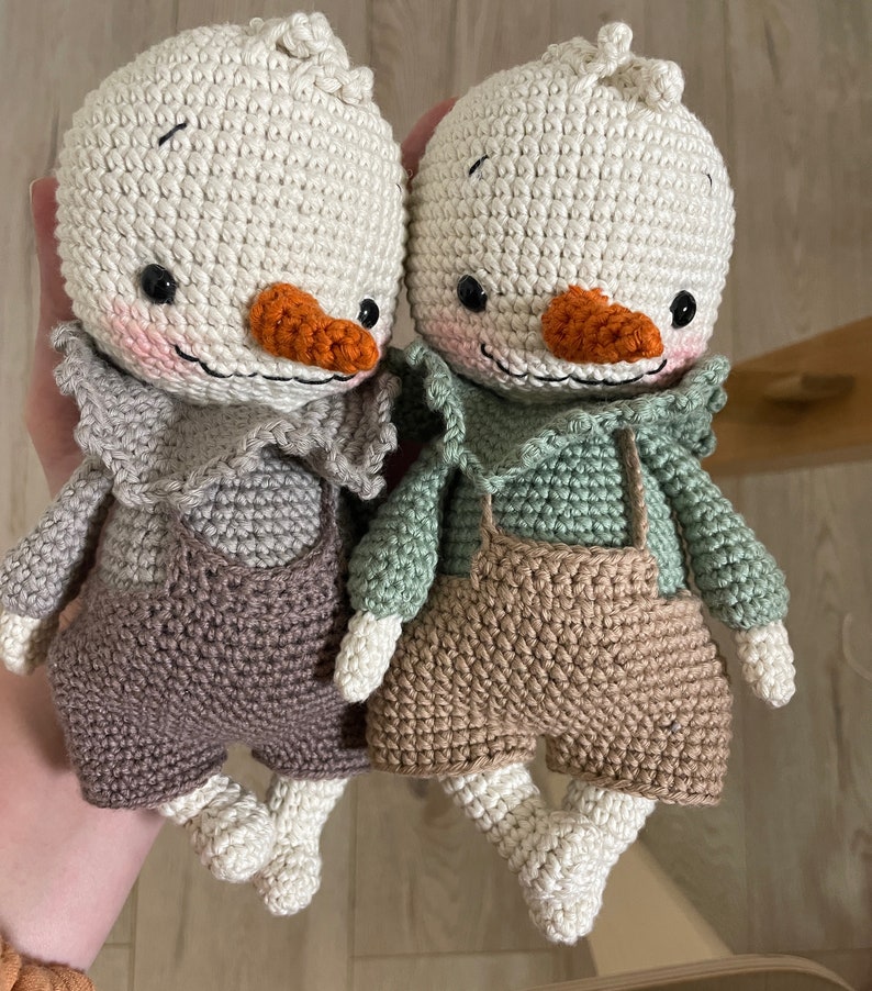 May include: Two crocheted stuffed toys shaped like birds with brown and beige overalls. One bird has a green shirt and the other has a brown shirt.