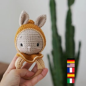 May include: A crocheted bunny rattle toy with a brown and beige color scheme. The rattle has a wooden ring and is perfect for a baby's small hands.