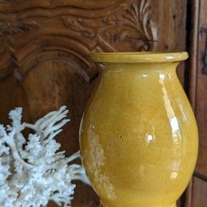 May include: A yellow ceramic vase with a rounded body and a wide mouth. The vase is sitting on a wooden surface.