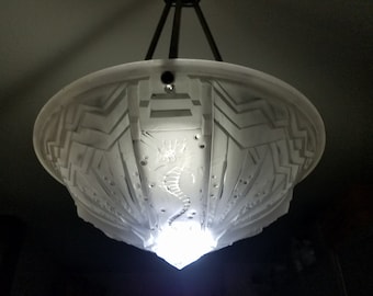 May include: White frosted glass ceiling light fixture with an intricate geometric design and a seahorse motif. The light is on and illuminating the room.