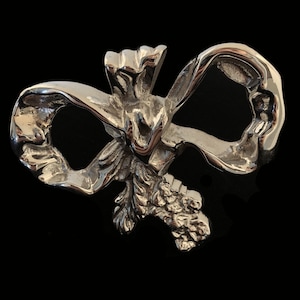 Może przedstawiać: Srebrna broszka w kształcie kokardki z kwiatowym wzorem. Kokardka jest zawiązana węzłem i ma szczegółową, fakturowaną powierzchnię.