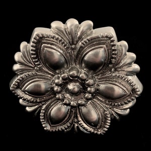 Peut inclure: Un bouton en métal argenté en forme de fleur avec un design détaillé. Le bouton a un cercle central entouré de petits cercles, et les bords extérieurs sont en forme de pétales.