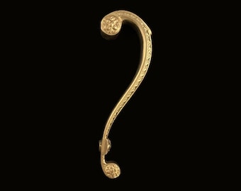 May include: A gold-colored metal door handle with a decorative design. The handle is shaped like a question mark and has a floral pattern.