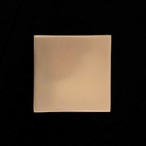 Può includere: Una piastrella quadrata in metallo spazzolato di colore oro chiaro.