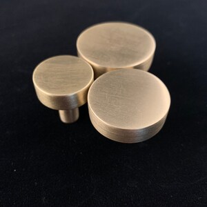 May include: Three round, brushed gold cabinet knobs of different sizes.