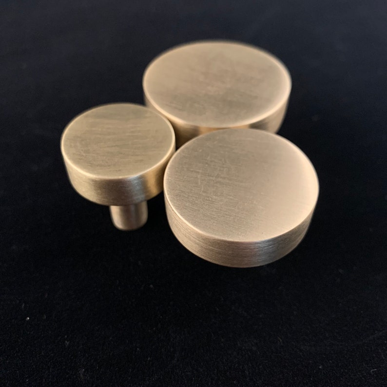 May include: Three round, brushed gold cabinet knobs of different sizes.