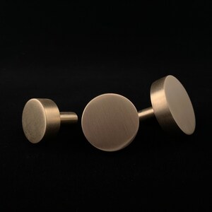 May include: Three round, brushed brass cabinet knobs. The knobs are different sizes, with the largest knob being about 2 inches in diameter.